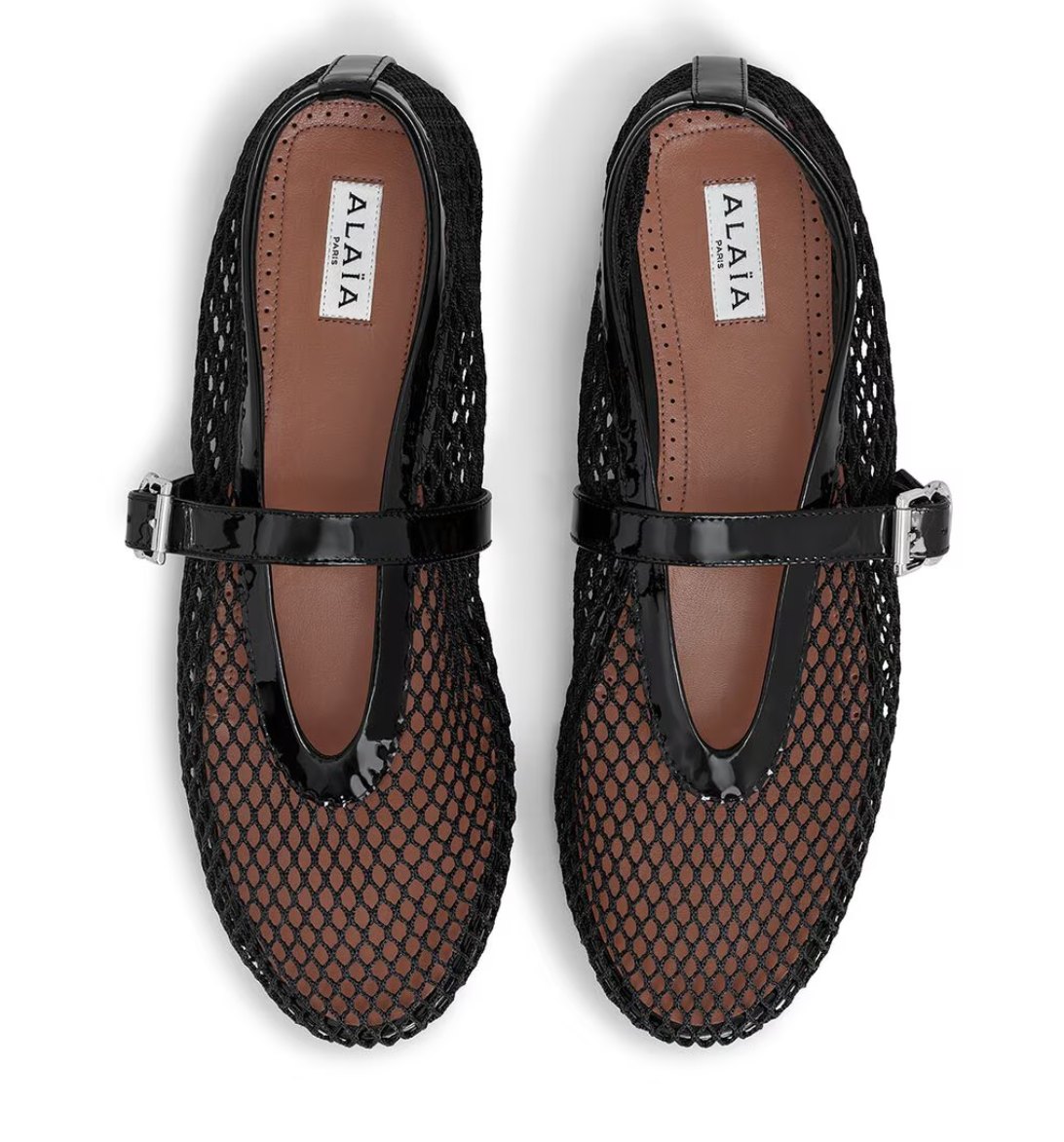 A pair of black fishnet Alaia ballet flats with patent Mary Jane straps, photographed from above, official product image