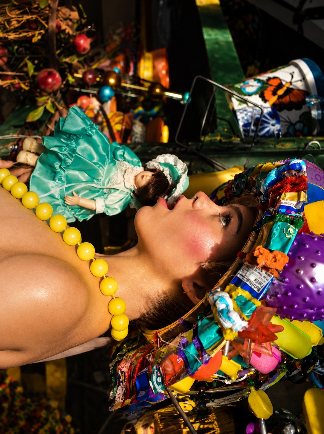 Reclining figure with a porcelain doll and a headpiece built from wrappers and plastic toys