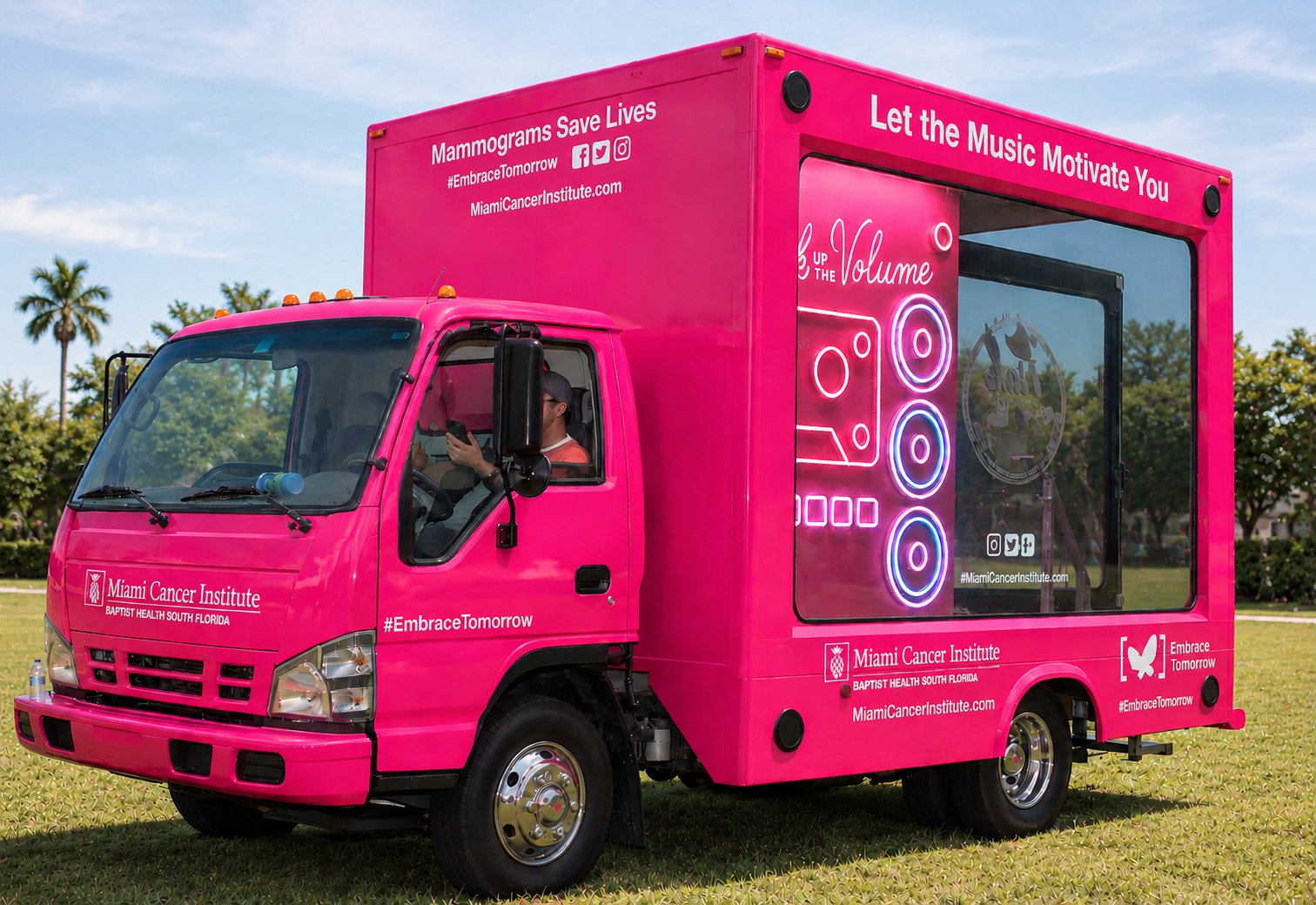 A bright pink Miami Cancer Institute mobile mammography truck parked on grass, reading Mammograms Save Lives