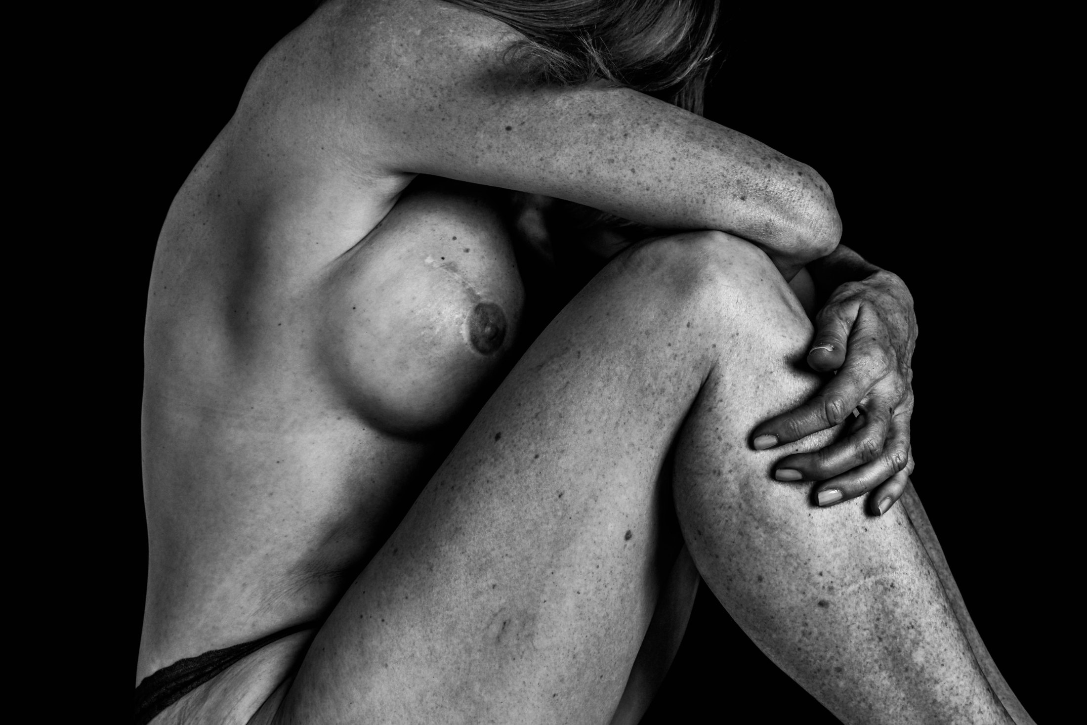 Black and white photograph, figure with knees drawn up