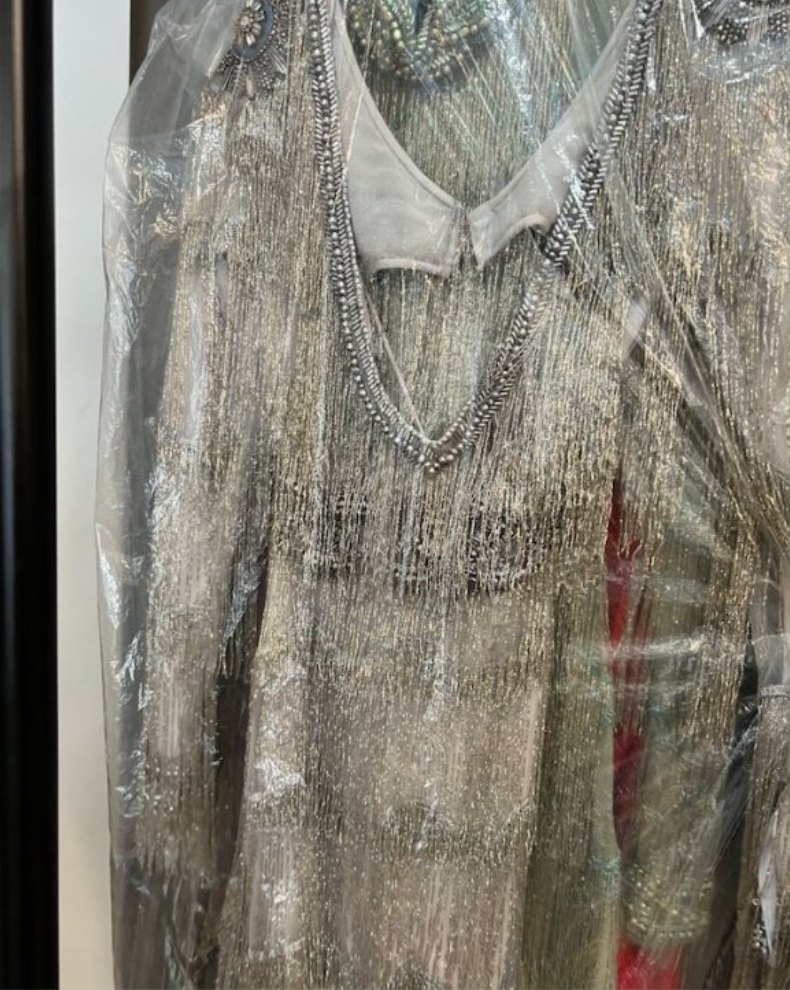 A beaded silver fringe dress bagged in plastic on a rack
