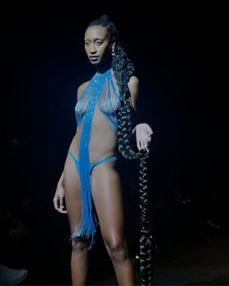 A model on a dark runway in a blue beaded fringe look holding a long braid