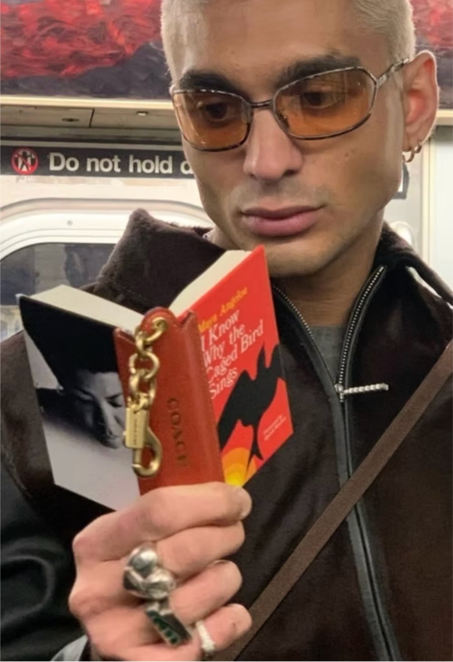 A man on the subway holding a miniature leather Coach charm of I Know Why the Caged Bird Sings beside the real book