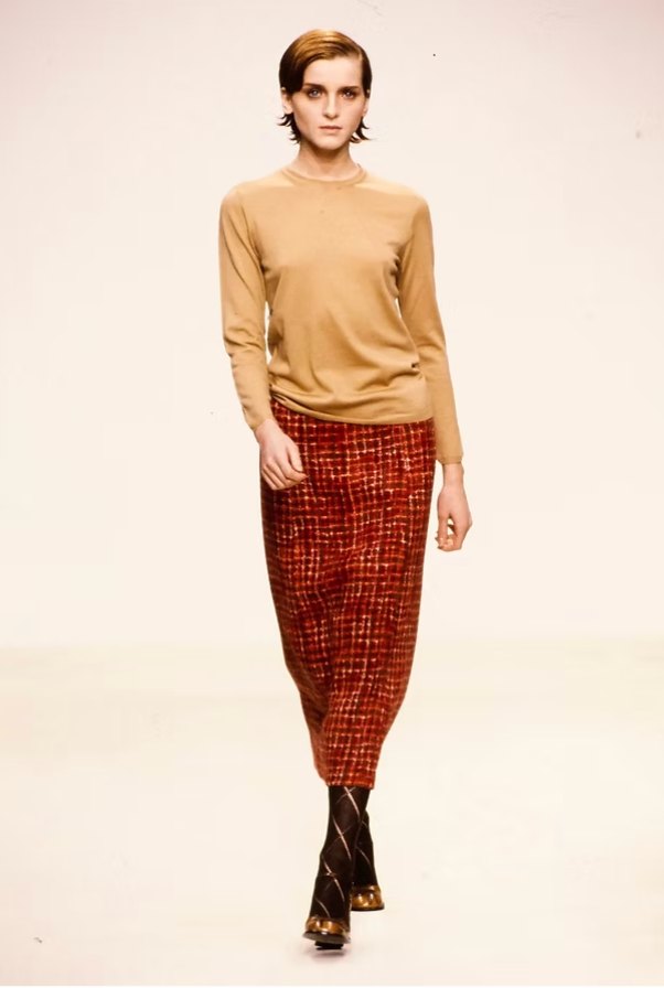 A Prada look of a camel crewneck sweater with a russet check pencil skirt and patterned socks