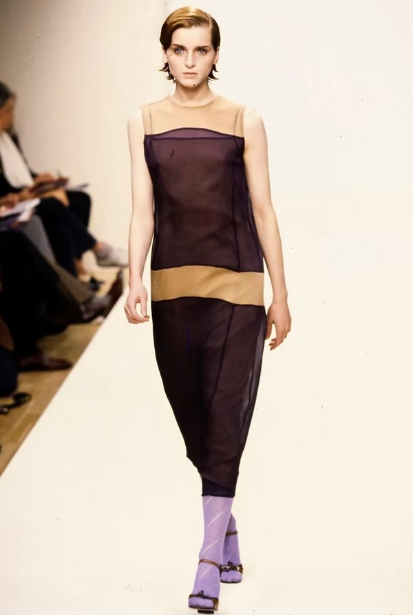 A Prada look of a sheer aubergine sleeveless dress over a nude underlayer with lilac socks and sandals